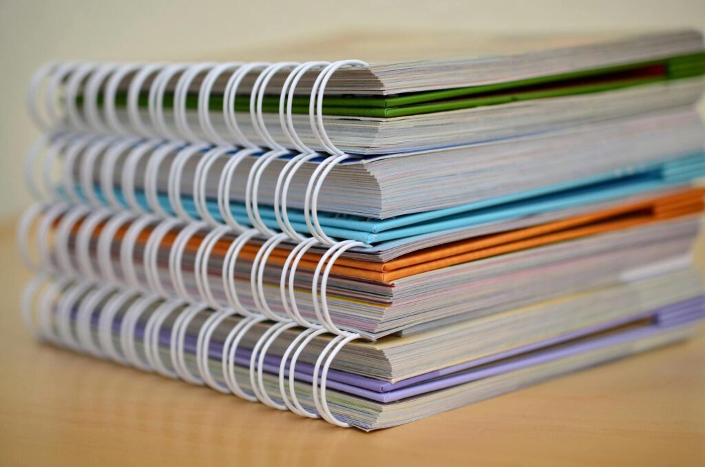 Pila de cuadernos con encuadernación de espiral y cubiertas de distintos colores colocados sobre una mesa.