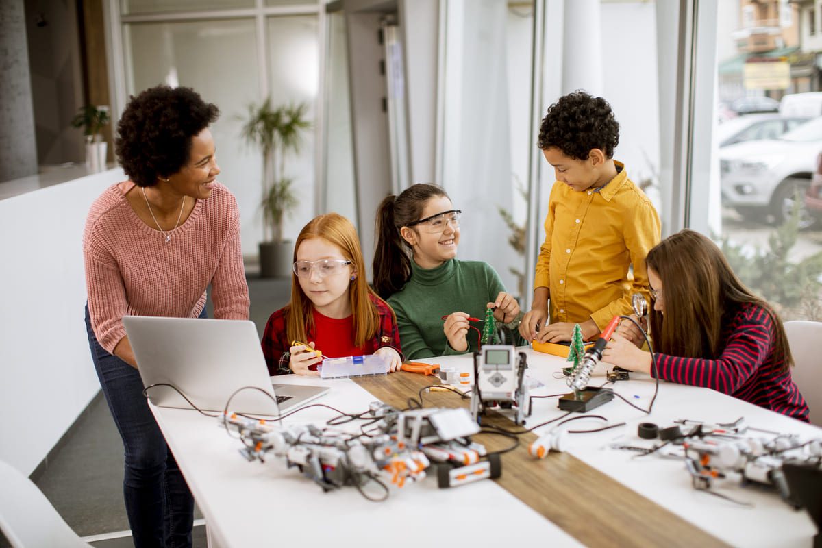 Niños participando en una actividad educativa con tecnología y robótica junto a una profesora en el aula escolar.