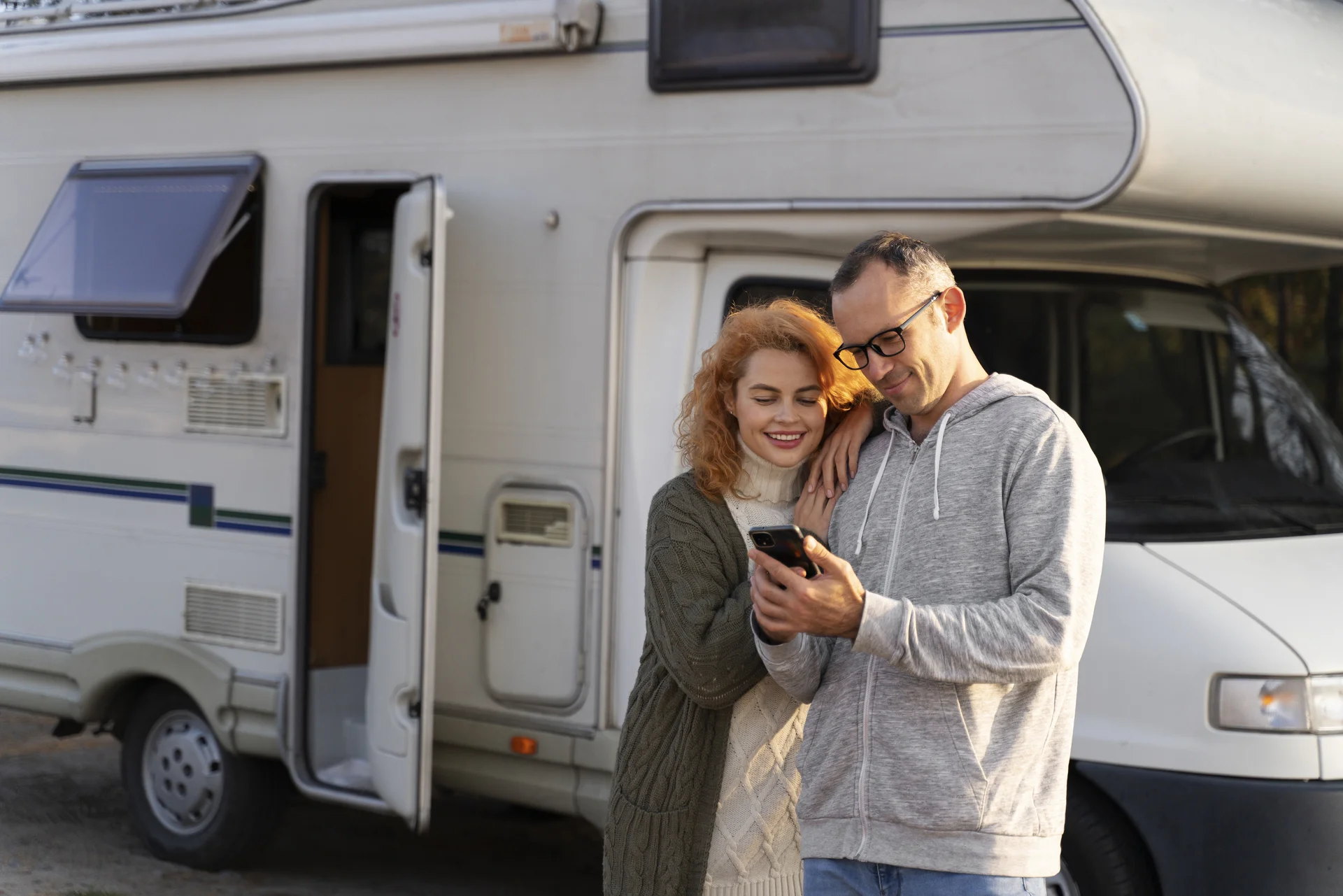 Pareja consultando el móvil junto a una autocaravana durante un viaje por carretera
