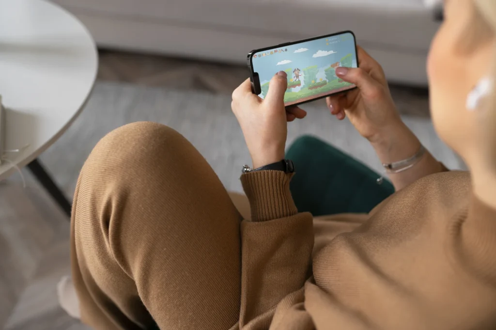 Persona jugando a un videojuego en un smartphone sostenido en posición horizontal mientras está sentada en casa