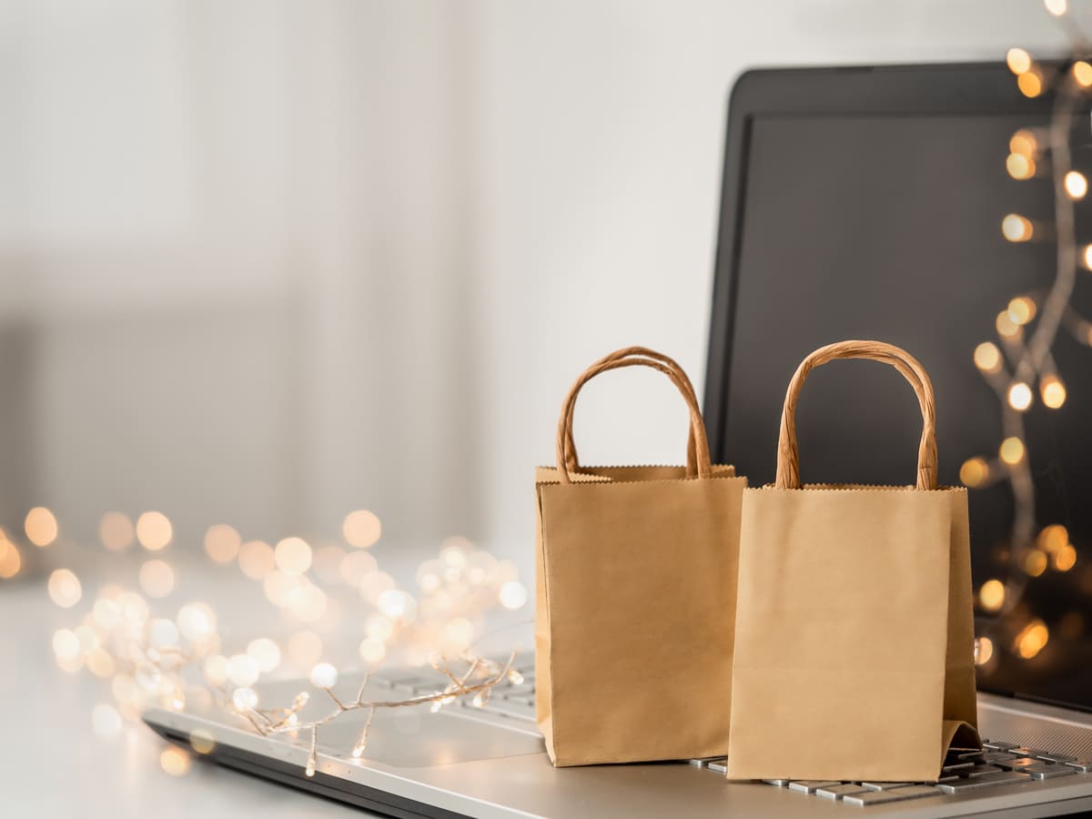Dos bolsas de papel kraft sobre el teclado de una laptop, junto a una guirnalda de luces cálidas desenfocadas